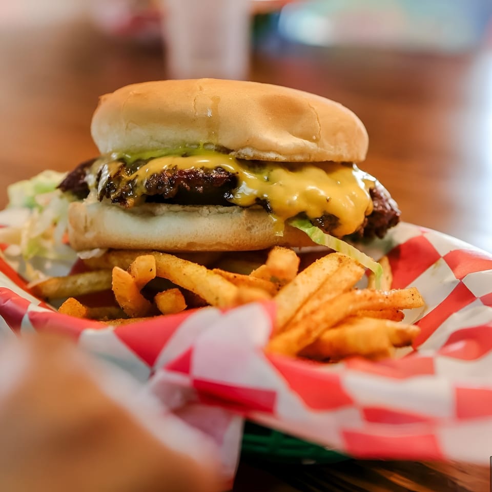 Cheeseburger with melted cheese, lettuce, and sauce, served with golden fries in a red and white checkered basket.