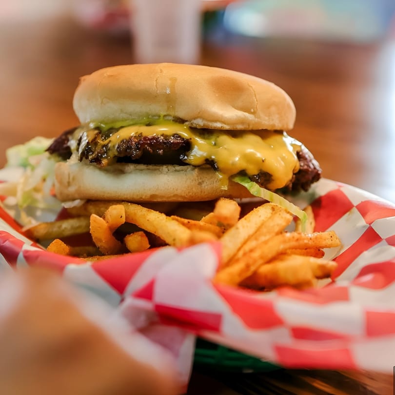 Cheeseburger with melted cheese, lettuce, and sauce, served with golden fries in a red and white checkered basket.