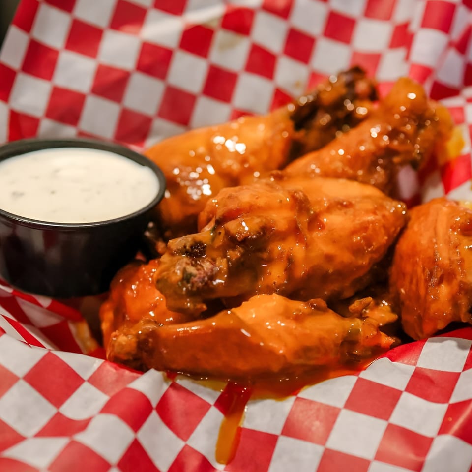 Buffalo chicken wings with ranch dressing in a red and white checkered basket.