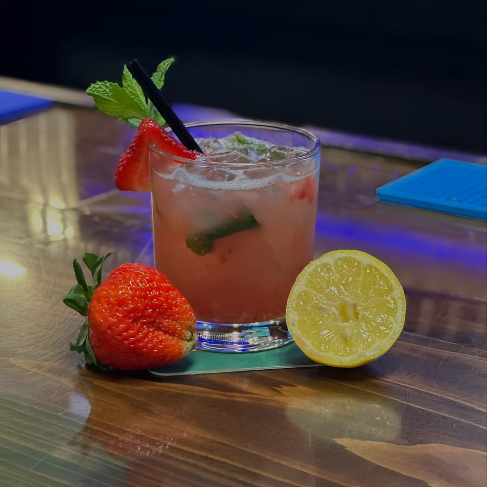 Strawberry mojito with mint, a whole strawberry, and a lemon half on a wooden table.