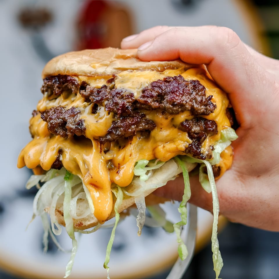 Hand holding a double smash burger with melted cheese, shredded lettuce, and special sauce.