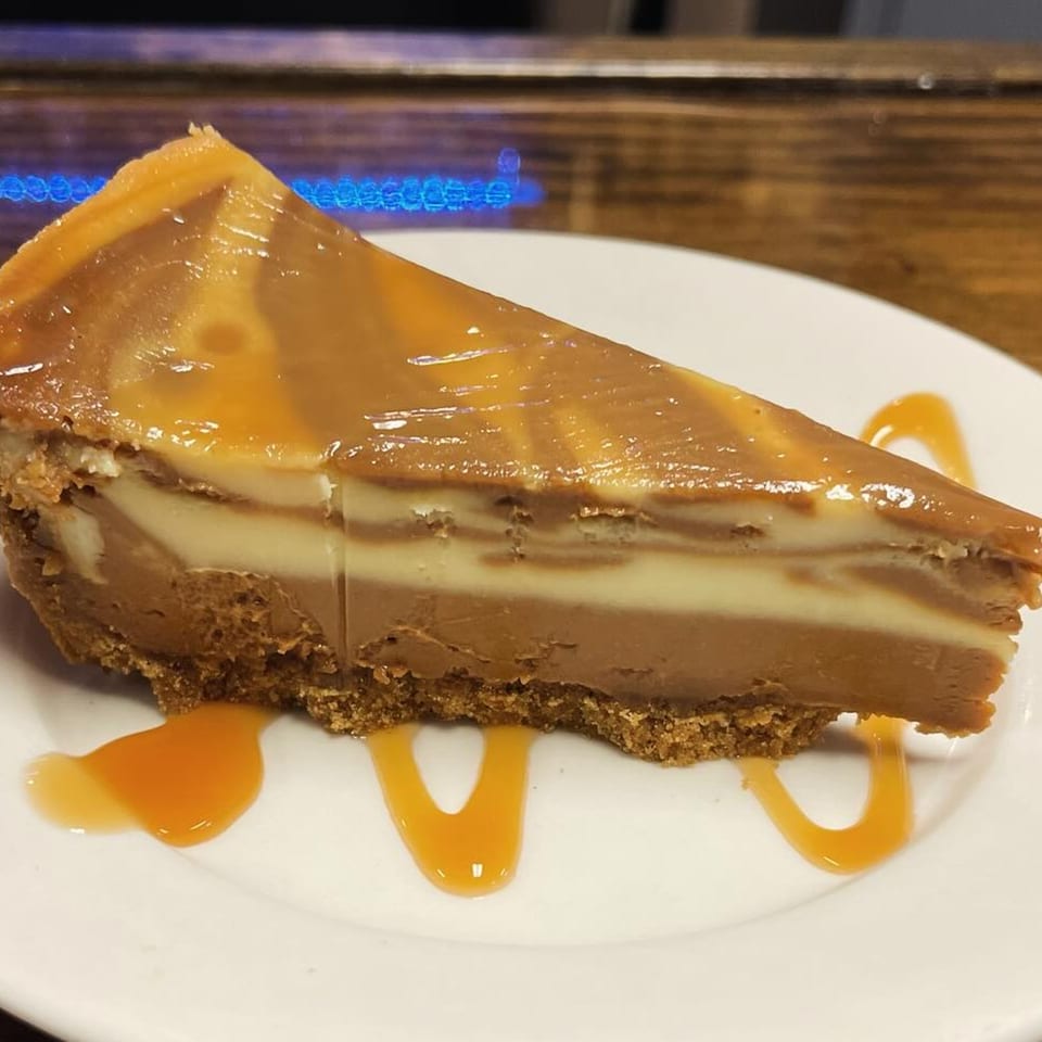 A slice of caramel cheesecake with a graham cracker crust and caramel drizzle on a white plate.