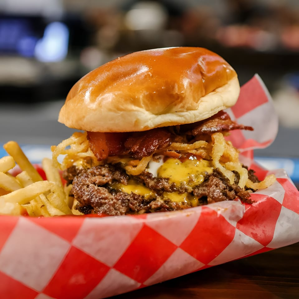 A juicy double cheeseburger with bacon, crispy onions, and fries in a red checkered basket.